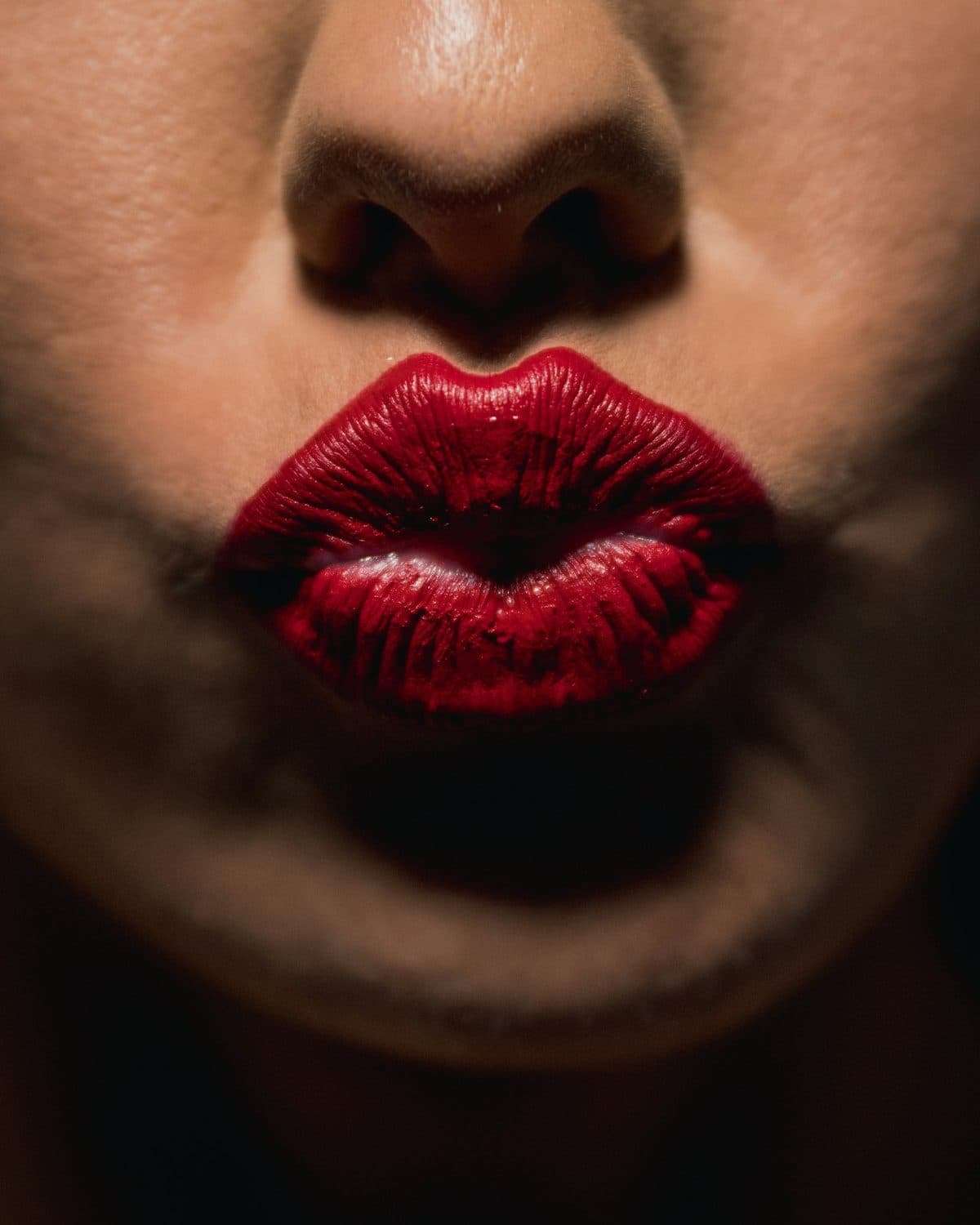 A deep red lip, lit close against the dark